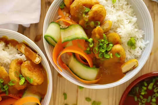 Chopped Quorn Crispy Nuggets served on a bed of rice, cucumber and carrot in a bowl topped with katsu curry sauce and spring onions.