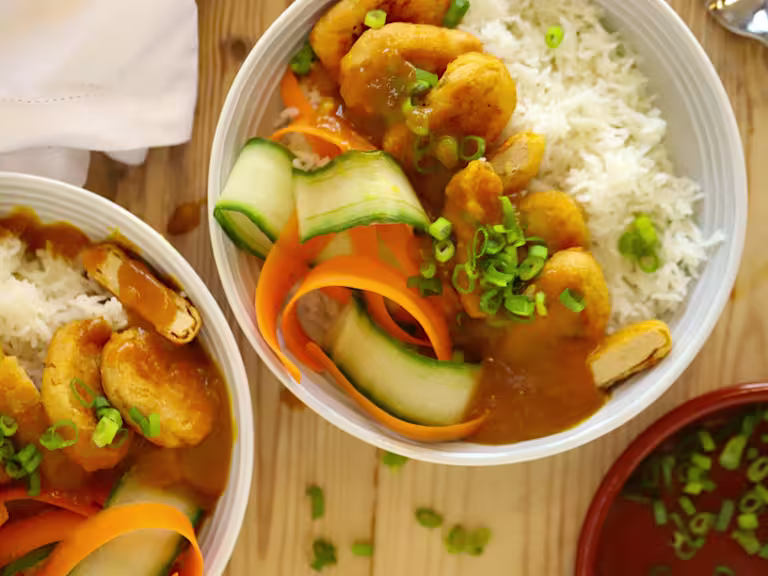 Chopped Quorn Crispy Nuggets served on a bed of rice, cucumber and carrot in a bowl topped with katsu curry sauce and spring onions.