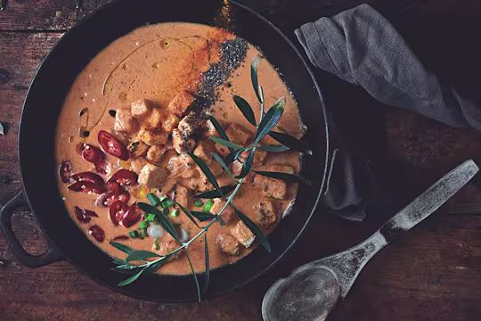 Vegetarian Thai red curry made with Quorn Pieces served in a bowl topped with red chilli and herbs with a spoon on the side