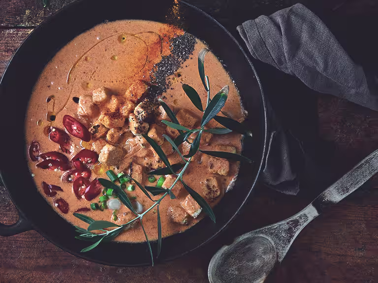 Vegetarian Thai red curry made with Quorn Pieces served in a bowl topped with red chilli and herbs with a spoon on the side
