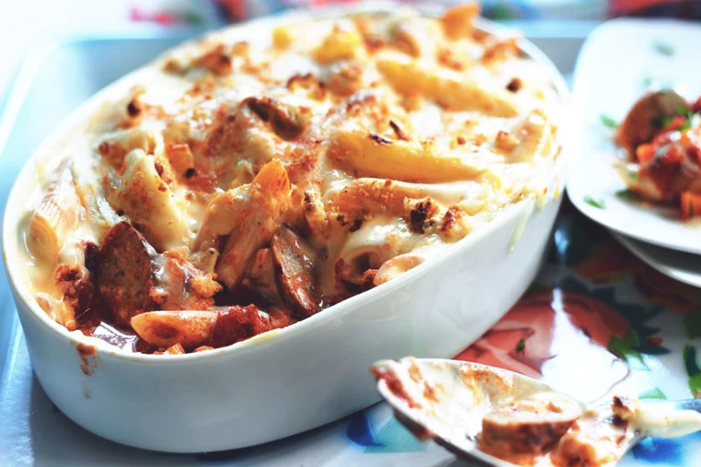 A white dish of penne pasta bake with Quorn Sausage topped with breadcrumbs and cheese.
