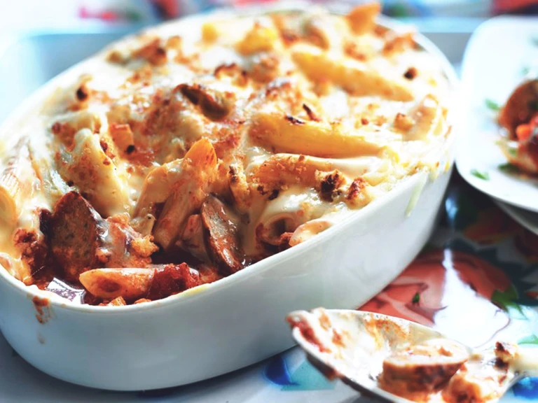 A white dish of penne pasta bake with Quorn Sausage topped with breadcrumbs and cheese.