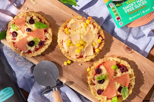 Mini cauliflower pizzas on wooden board positioned next to Quorn Vegan Ham Slices