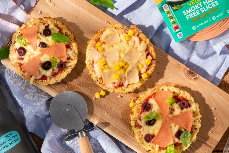 Mini cauliflower pizzas on wooden board positioned next to Quorn Vegan Ham Slices