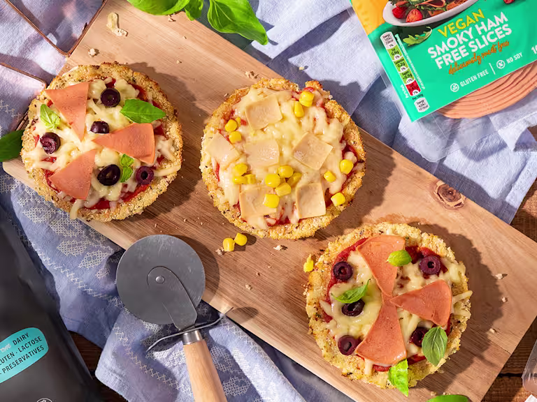 Mini cauliflower pizzas on wooden board positioned next to Quorn Vegan Ham Slices
