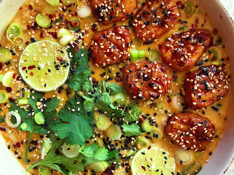 Coconut Noodle Soup with sticky sriracha Quorn Pieces visible, served alongside sliced lime and coriander.