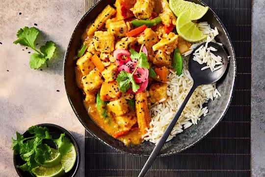 Quorn pieces in vegetarian slow cooker chicken curry served with white rice and lime wedges in a black bowl.