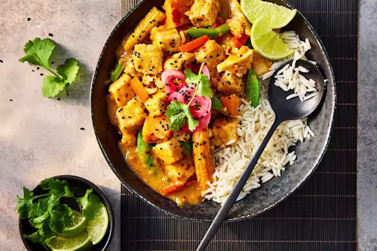 Quorn pieces in vegetarian slow cooker chicken curry served with white rice and lime wedges in a black bowl.