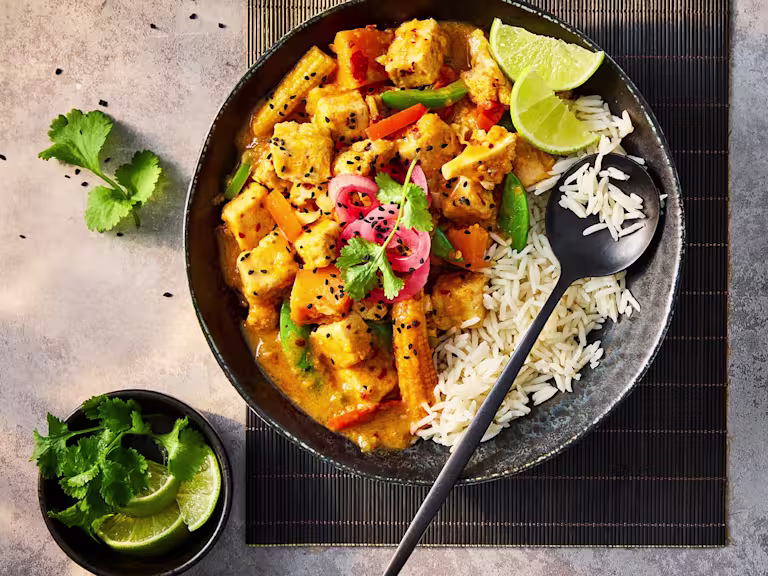 Quorn pieces in vegetarian slow cooker chicken curry served with white rice and lime wedges in a black bowl.