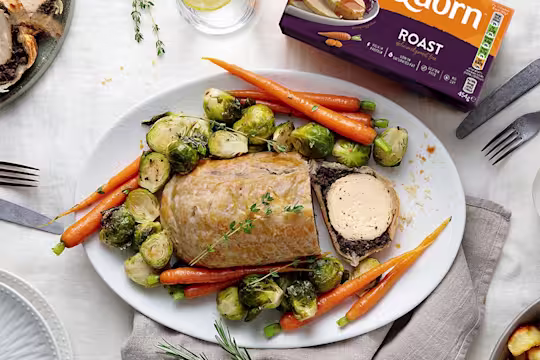 A vegetarian wellington made with Quorn Roast wrapped in mushrooms duxelles and puff pastry surrounded by roasted brussels sprouts and carrots with roast potatoes on the side.