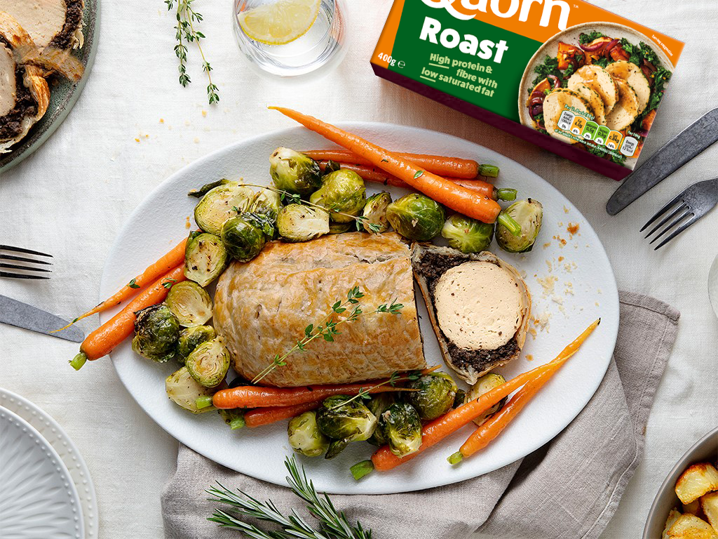 A vegetarian wellington made with Quorn Roast wrapped in mushrooms duxelles and puff pastry surrounded by roasted brussels sprouts and carrots with roast potatoes on the side.