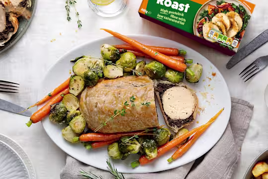 A vegetarian wellington made with Quorn Roast wrapped in mushrooms duxelles and puff pastry surrounded by roasted brussels sprouts and carrots with roast potatoes on the side.