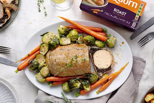A vegetarian wellington made with Quorn Roast wrapped in mushrooms duxelles and puff pastry surrounded by roasted brussels sprouts and carrots with roast potatoes on the side.