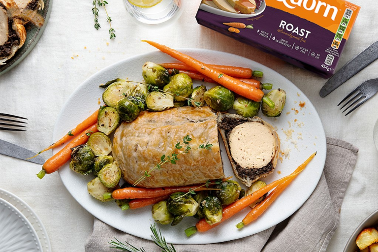 A vegetarian wellington made with Quorn Roast wrapped in mushrooms duxelles and puff pastry surrounded by roasted brussels sprouts and carrots with roast potatoes on the side.