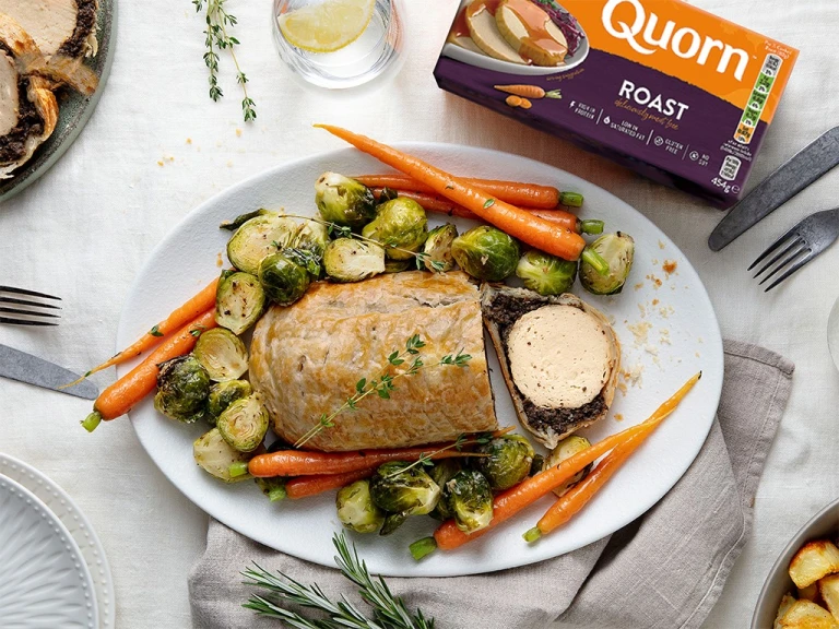 A vegetarian wellington made with Quorn Roast wrapped in mushrooms duxelles and puff pastry surrounded by roasted brussels sprouts and carrots with roast potatoes on the side.