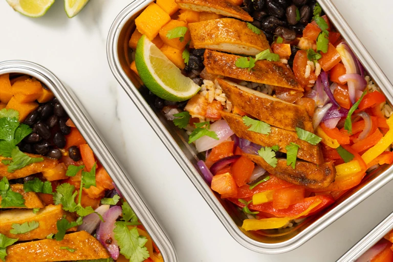 Vegetables, black beans and Quorn fillets served in a steel tin with sliced limes on the side.