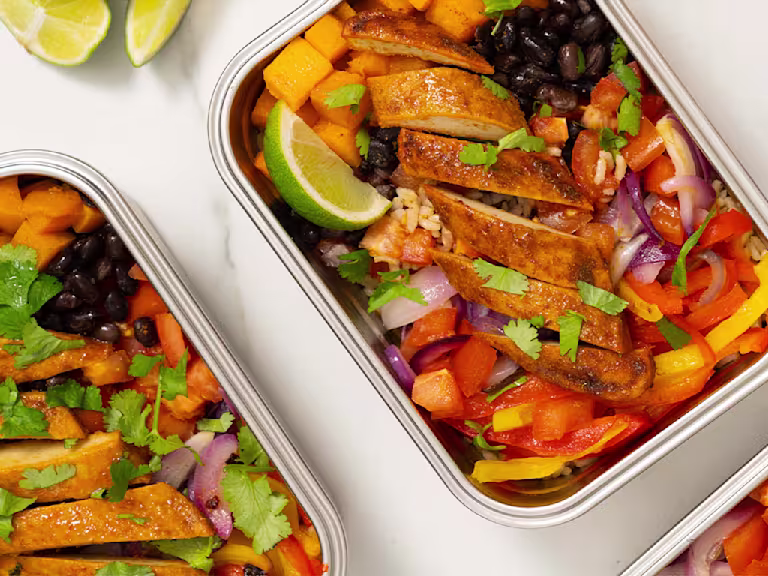 Vegetables, black beans and Quorn fillets served in a steel tin with sliced limes on the side.