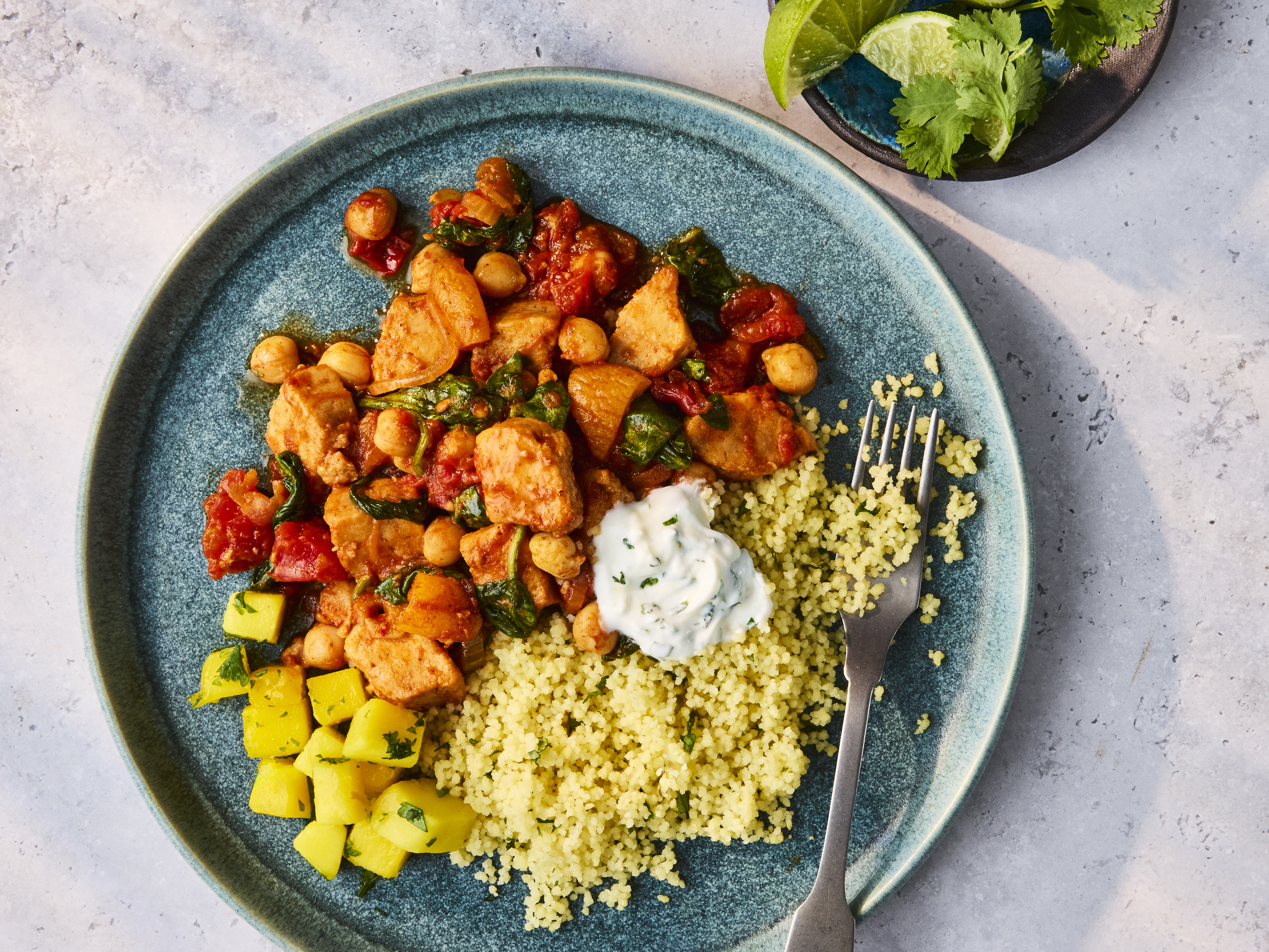 Plated Quorn Pieces Tagine with couscous, herbed yogurt, and a side of mango salad.