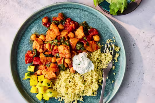 Plated Quorn Pieces Tagine with couscous, herbed yogurt, and a side of mango salad.