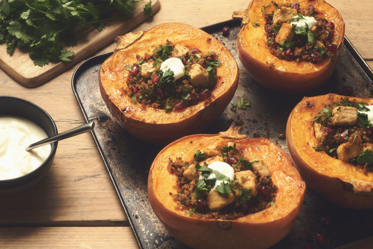 Four small pumpkins halved and baked stuffed with Quorn Pieces and quinoa, topped with yogurt and parsley on a baking sheet.