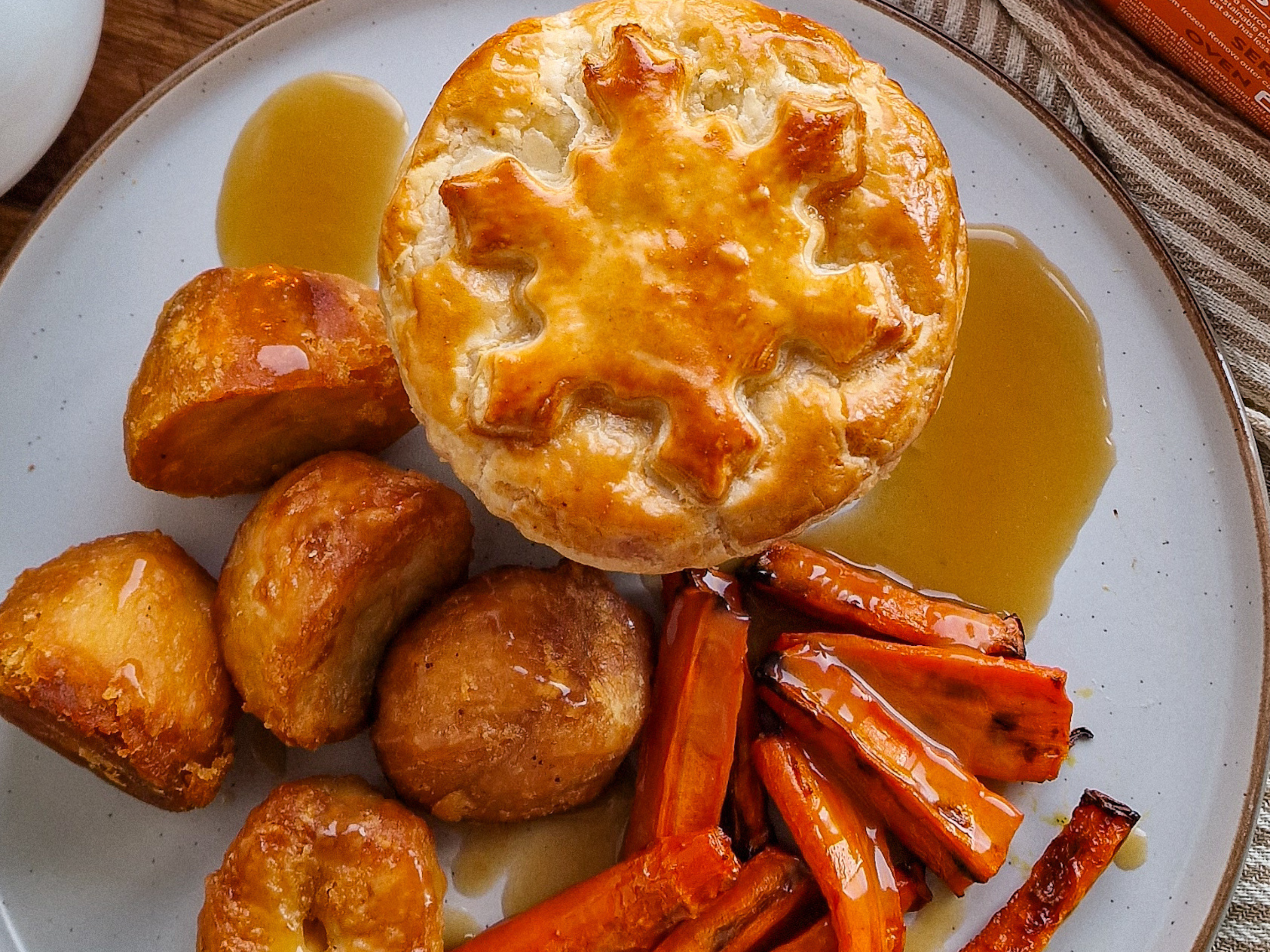 A Mini Festive Vegetarian Pie with potatoes, carrots and gravy on a white plate.