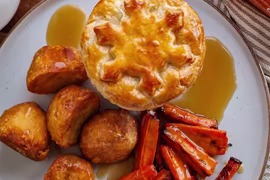 A Mini Festive Vegetarian Pie with potatoes, carrots and gravy on a white plate.