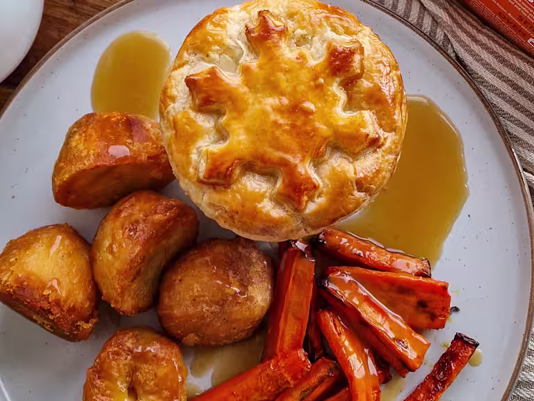 A Mini Festive Vegetarian Pie with potatoes, carrots and gravy on a white plate.