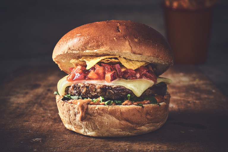 Veggie burger made with Quorn Classic Beef Style Burger topped with cheese, relish and nachos sandwiched between a bun