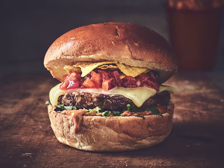 Veggie burger made with Quorn Quarter Pounders topped with cheese, relish and nachos sandwiched between a bun