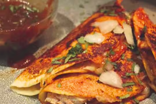 Vegetarian Birria tacos topped with herbs and onions next to a bowl of sauce.