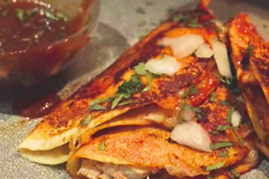 Vegetarian Birria tacos topped with herbs and onions next to a bowl of sauce.