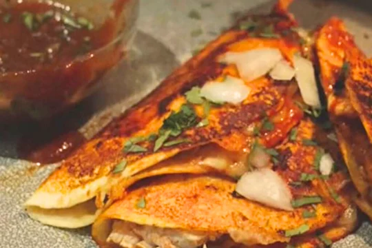 Vegetarian Birria tacos topped with herbs and onions next to a bowl of sauce.