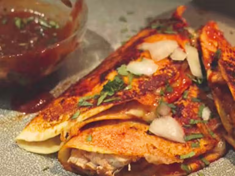 Vegetarian Birria tacos topped with herbs and onions next to a bowl of sauce.