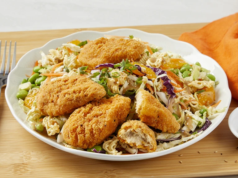 Ramen salad topped with Quorn meatless chicken wings with a bowl of peas served on the side.