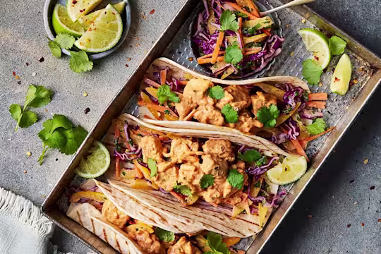 Three Vegetarian Chicken Lunch Wrap facing upwards to show the fillings of Quorn Vegetarian BBQ Chicken sandwich filler with a pot of coleslaw and sliced limes on the side.