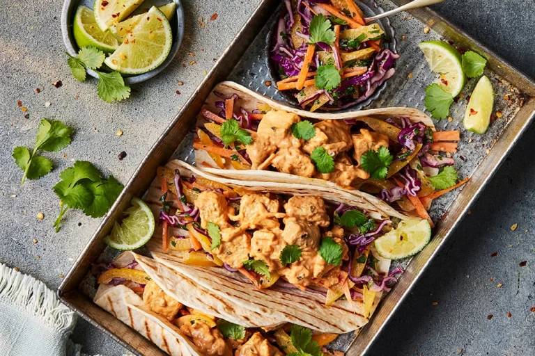 Three Vegetarian Chicken Lunch Wrap facing upwards to show the fillings of Quorn Vegetarian BBQ Chicken sandwich filler with a pot of coleslaw and sliced limes on the side. 