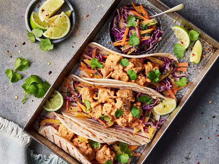 Three Vegetarian Chicken Lunch Wrap facing upwards to show the fillings of Quorn Vegetarian BBQ Chicken sandwich filler with a pot of coleslaw and sliced limes on the side.