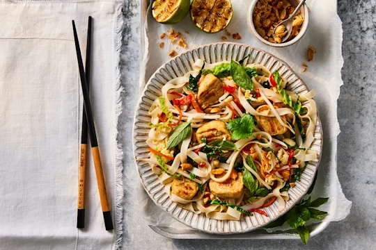 A bowl of Quorn Pad Thai made using Quorn Vegetarian Chicken Fillet Pieces next to a set of chopsticks.