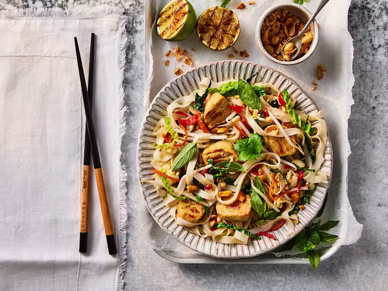 A bowl of Quorn Pad Thai made using Quorn Vegetarian Chicken Fillet Pieces next to a set of chopsticks.