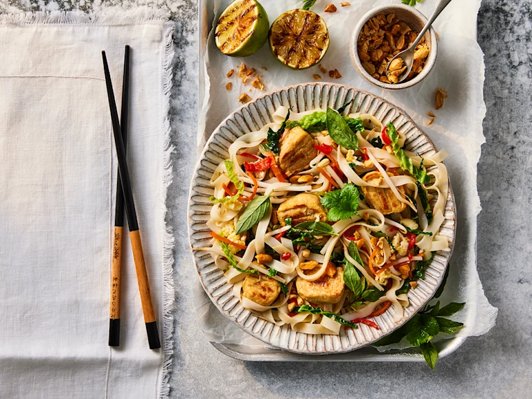 A bowl of Quorn Pad Thai made using Quorn Vegetarian Chicken Fillet Pieces next to a set of chopsticks.
