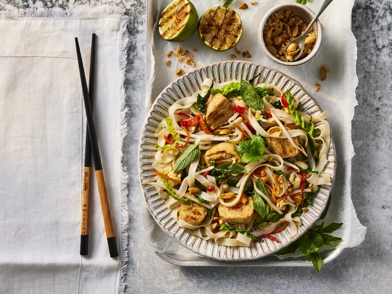 A bowl of Quorn Pad Thai made using Quorn Vegetarian Chicken Fillet Pieces next to a set of chopsticks.