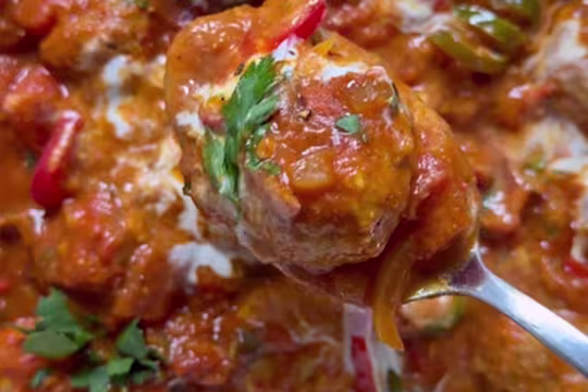 Quorn Swedish Style Meatball in a curry sauce on a spoon with chopped herb garnish and chillies.