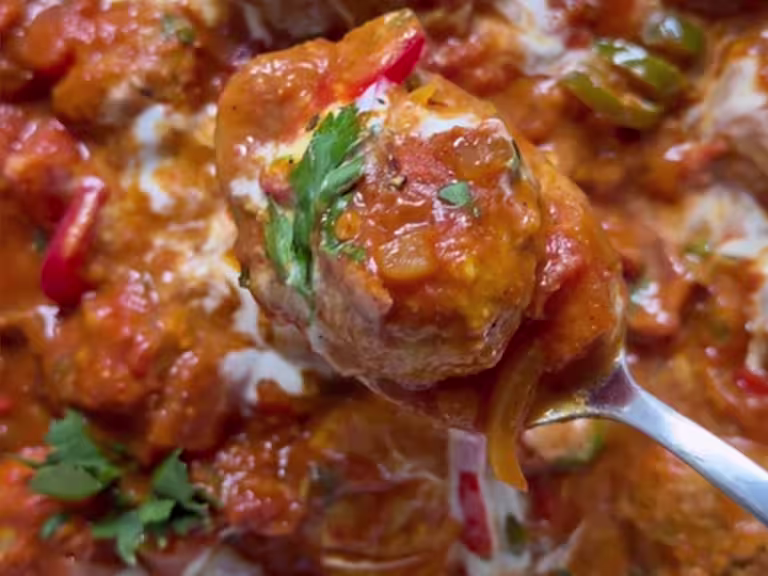 Quorn Swedish Style Meatball in a curry sauce on a spoon with chopped herb garnish and chillies.