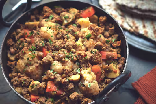 Meat free curry recipe made with Quorn Mince, cauliflower, carrots and lentils garnished with coriander served in a black pot