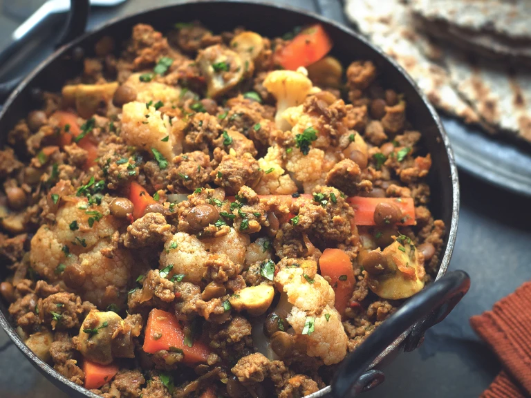 Meat free curry recipe made with Quorn Mince, cauliflower, carrots and lentils garnished with coriander served in a black pot