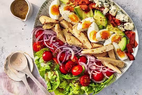 Layered salad on a ceramic plate with lettuce, chopped cherry tomatoes, sliced red onion, Quorn Roast Mini Fillets, sliced boiled egg, sliced avocado, grilled red pepper and cubes of blue cheese.