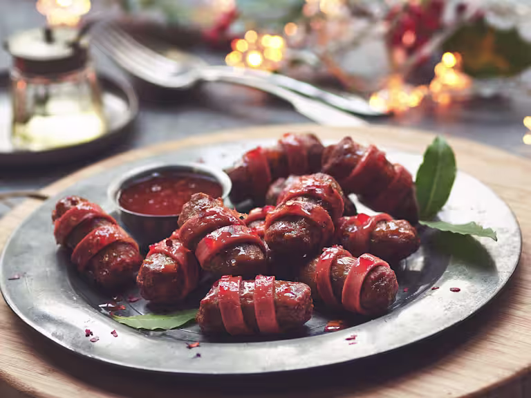 Vegetarian Pigs in Blankets made with Quorn Cocktail Sausage wrapped in Quorn Vegan Ham Slices on a plate with bay leaves and tomato sauce.