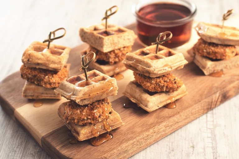 Vegetarian party food of meat free Quorn Crunchy Tex Mex Nuggets sandwiched between two waffles, all served on a wooden tray