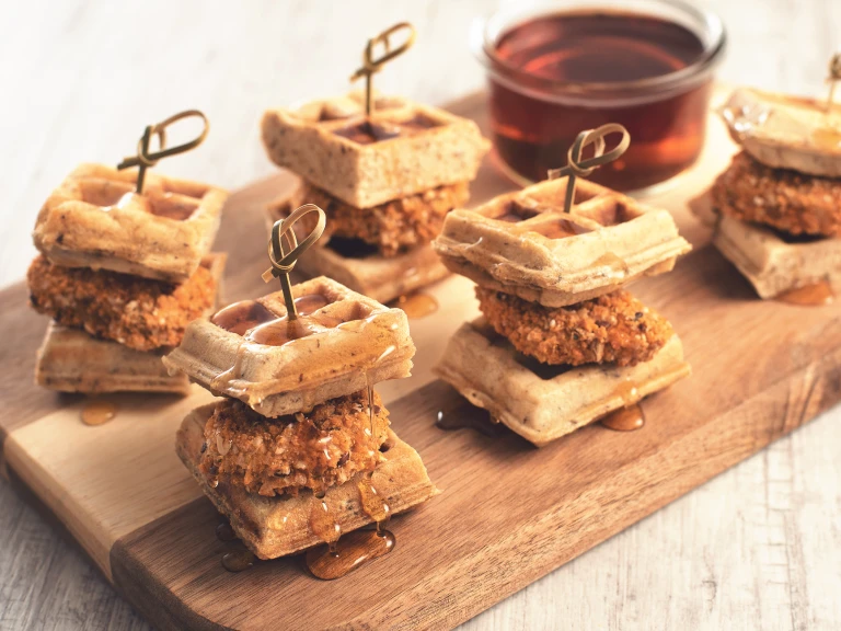 Vegetarian party food of meat free Quorn Crunchy Tex Mex Nuggets sandwiched between two waffles, all served on a wooden tray