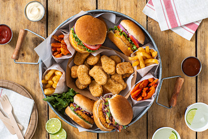 A Quorn Vegan Meatless Spicy Patty on the bottom of a burger bun topped with mixed greens, spicy beans, and a tomato relish on a slate tray with a small glass bowl of beans in the background.